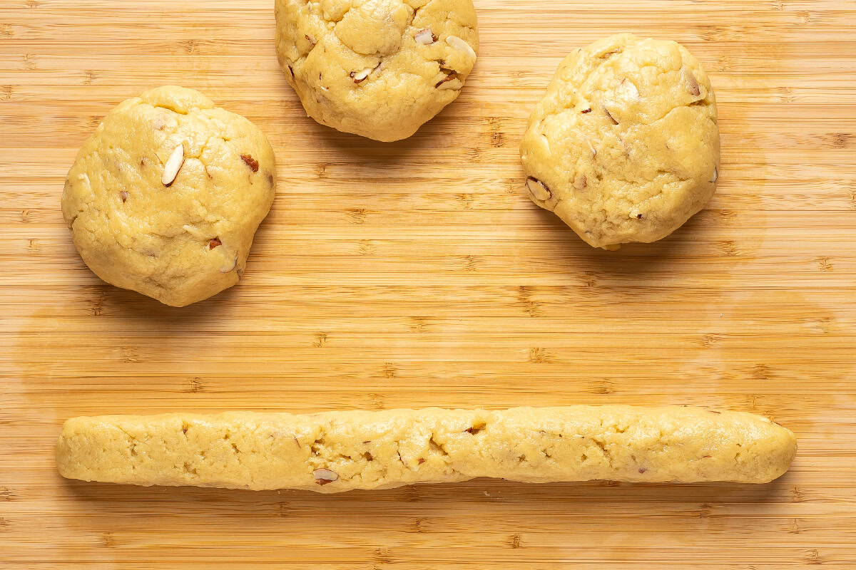 One log of dough with 3 dough balls on a wooden cutting board.
