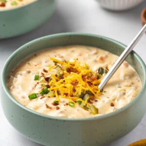 A green bowl of bacon cheeseburger soup topped with shredded cheese