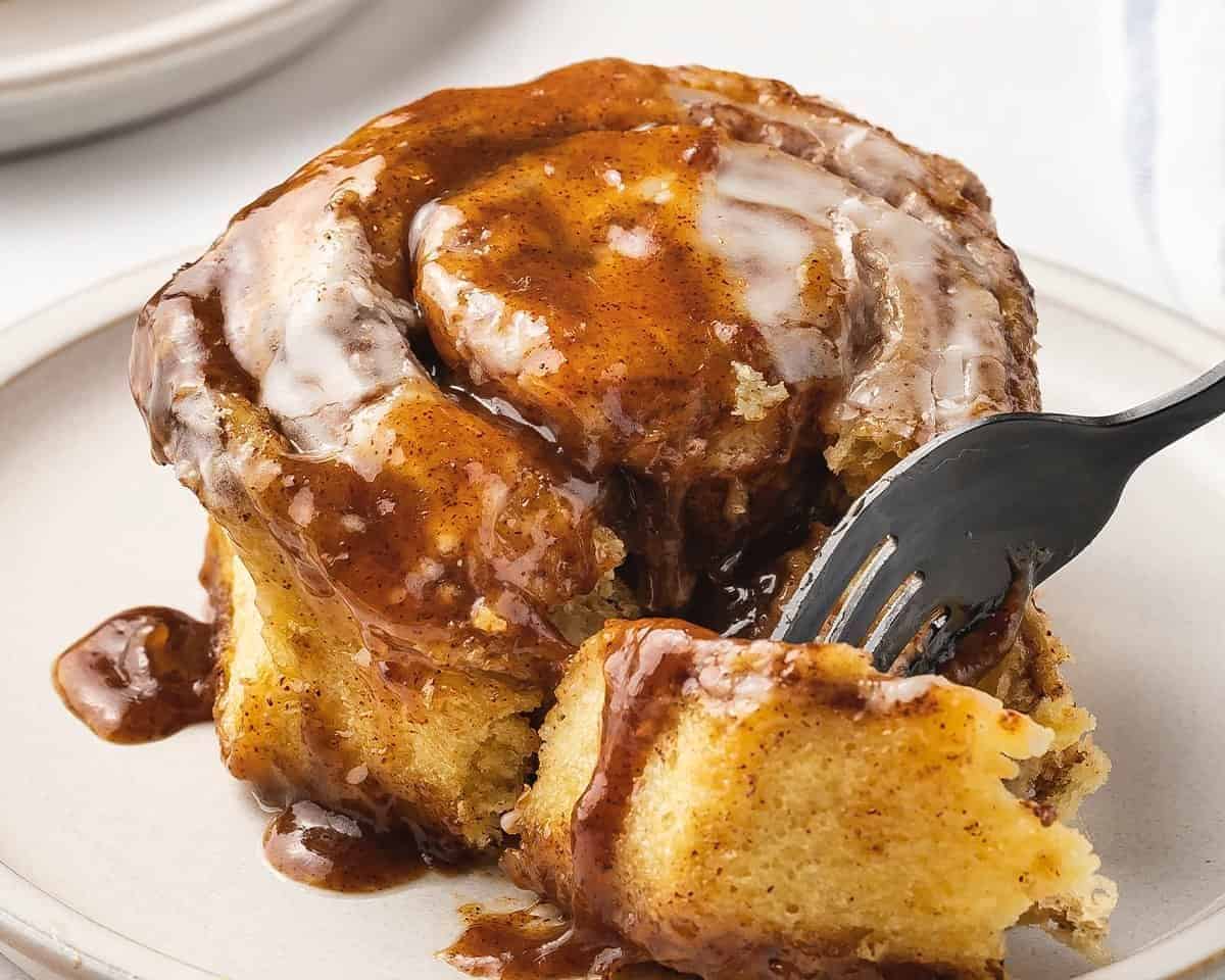Cinnamon roll with cinnamon brown sugar poured over it with a fork. 