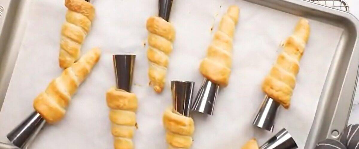 Baked creamed horns on a baking sheet on a cooling rack.