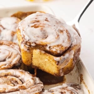 A spoon lifting out a cinnamon roll from a baking dish
