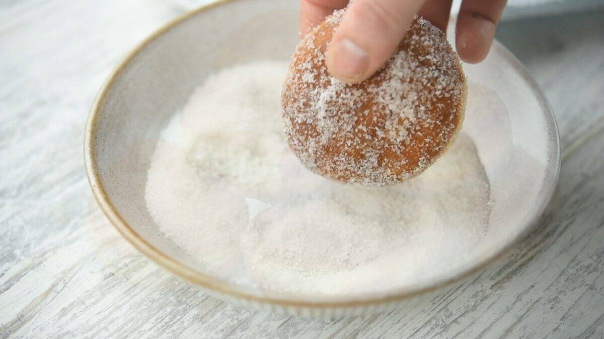 Dredging a donut in granulated sugar.