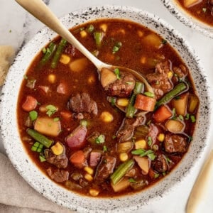 A spoon in a bowl of vegetable beef soup