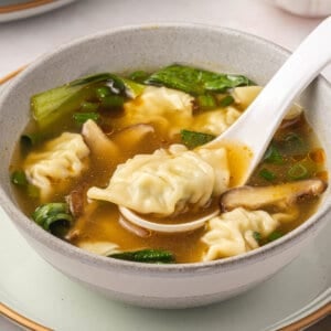 A bowl of homemade wonton soup with a white spoon