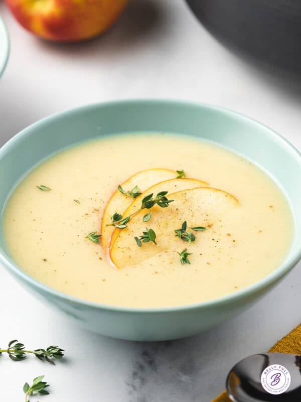 bowl of parsnip soup garnished with sliced apple and thyme leaves