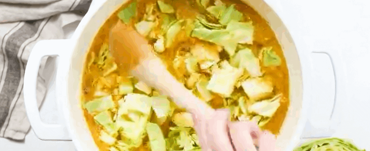 Adding chopped cabbage to the pot with the vegetables and broth.
