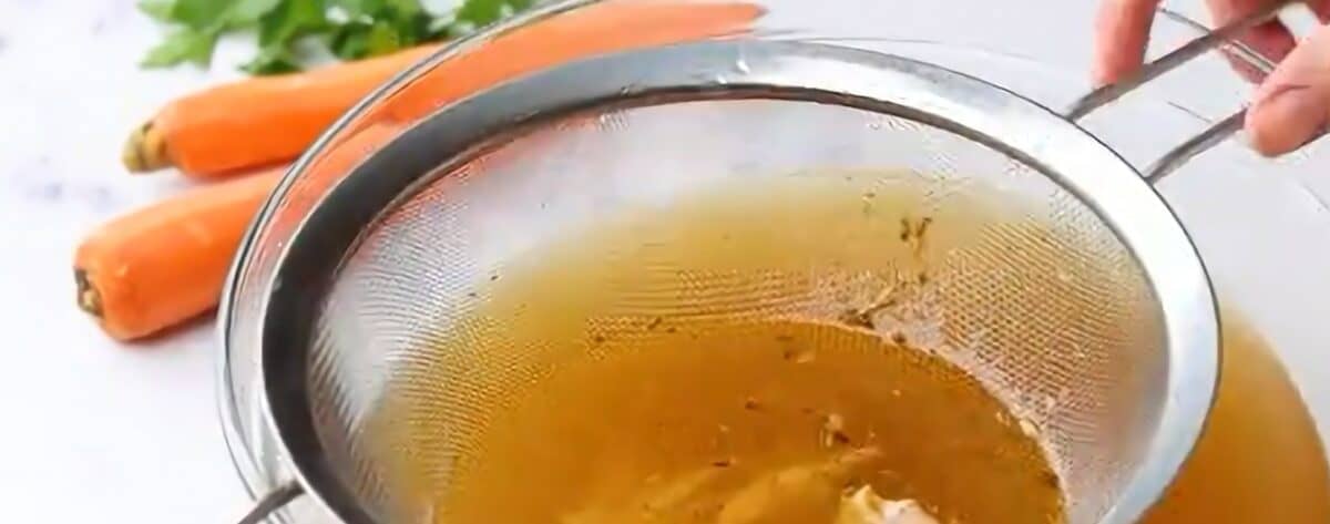 Straining the chicken broth through a mesh strainer.