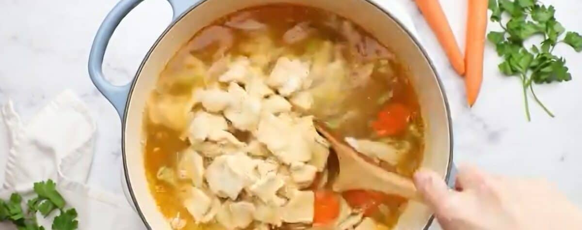 Adding the noodles to the pot with the veggies and broth. 