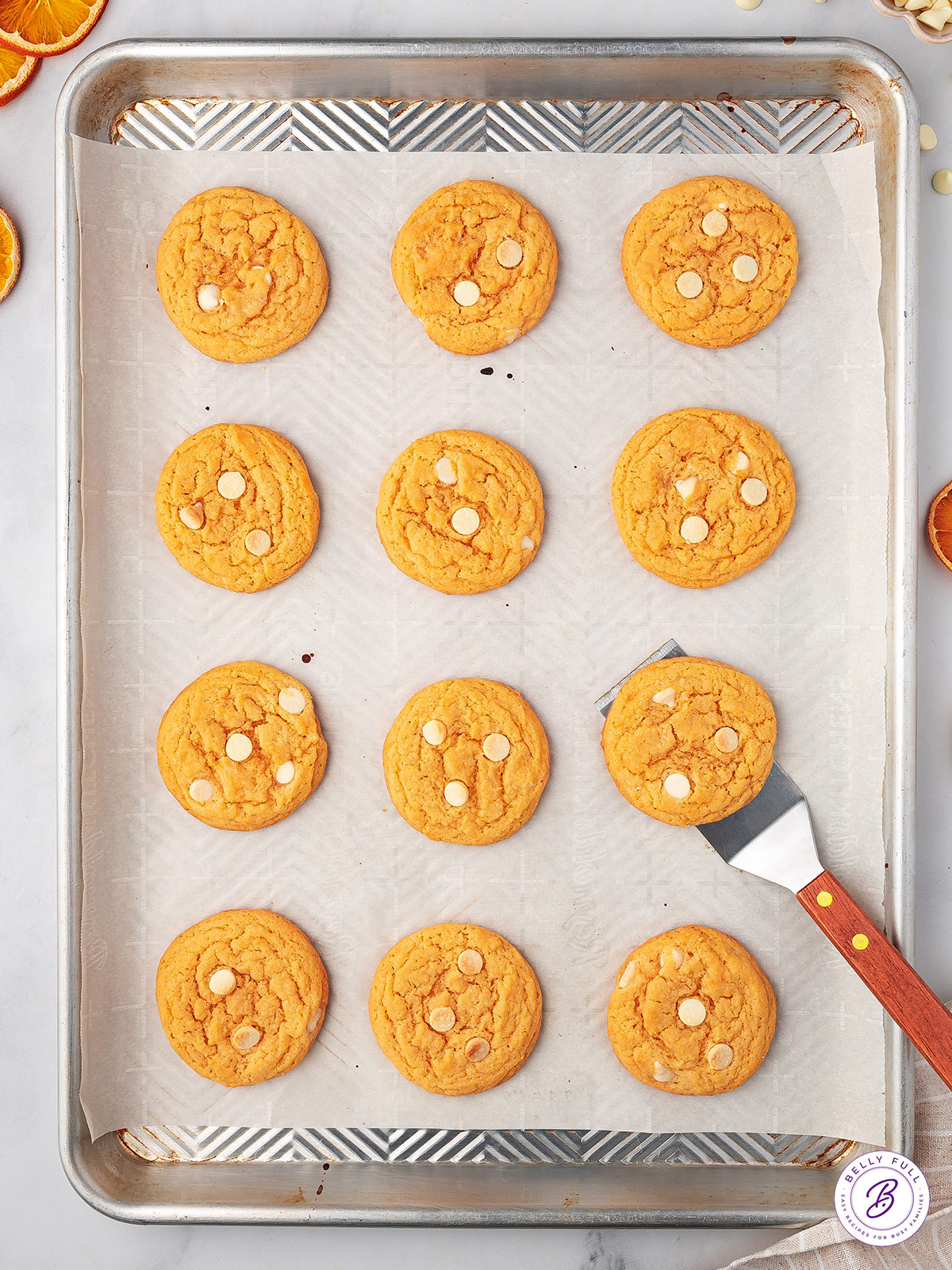 Overhead view of orange cookies with white chocolate chips on a baking sheet