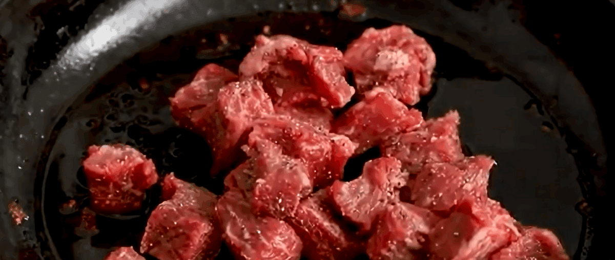 Cooking seasoned steak in a skillet.