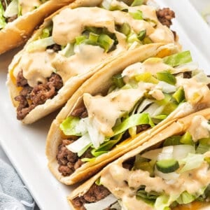 Tacos topped with shredded lettuce and Big Mac sauce on a white plate