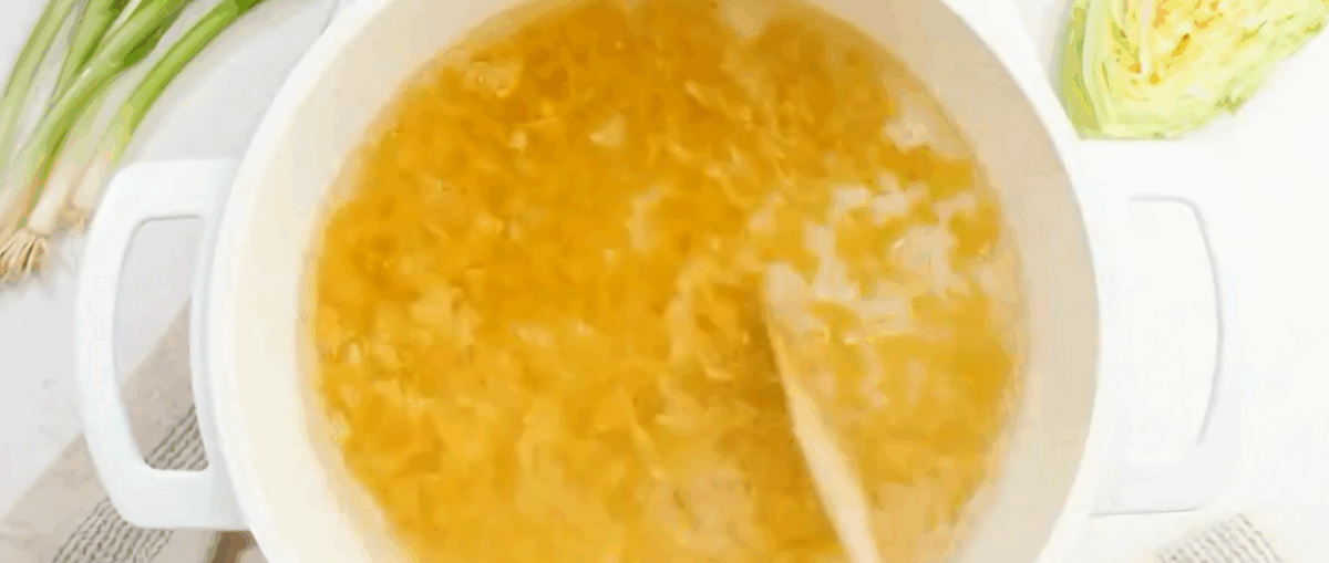 Cooking egg noodles in a white pot.