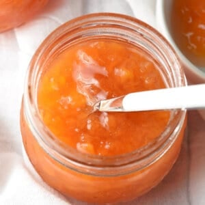 Peach jam in a glass jar with a spoon.
