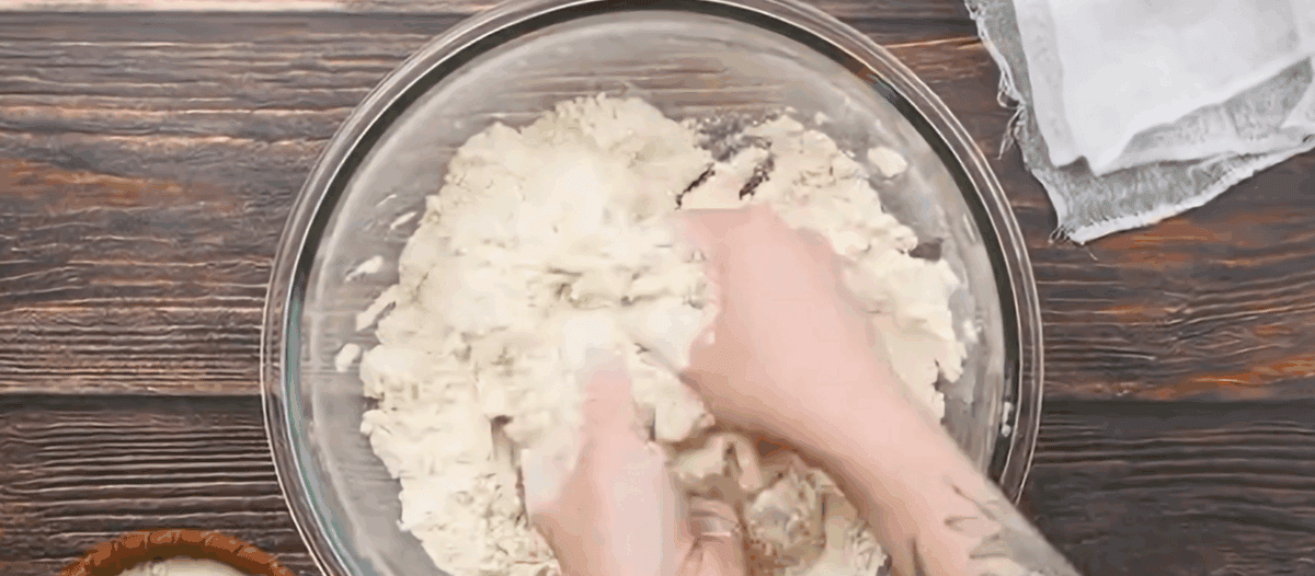 Hands combining the lard and flour in a glass bowl.