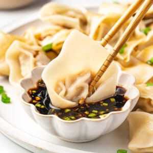 chopsticks dunking pork wonton into dipping sauce