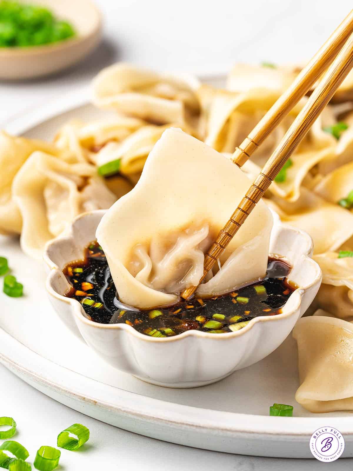 chopsticks dunking pork wonton into dipping sauce