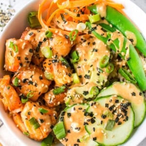 Overhead view of a salmon bowl with cucumbers, carrots, and snap peas