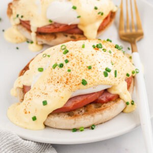 two portions of Eggs Benedict on white plate with fork