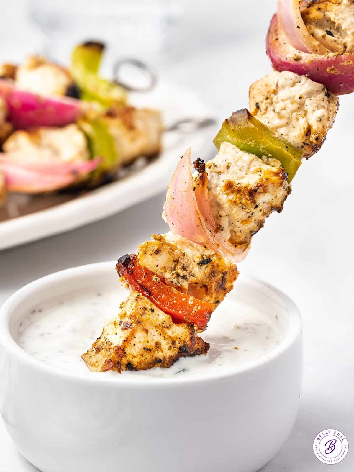 A Greek chicken skewer being dipped into tzatziki