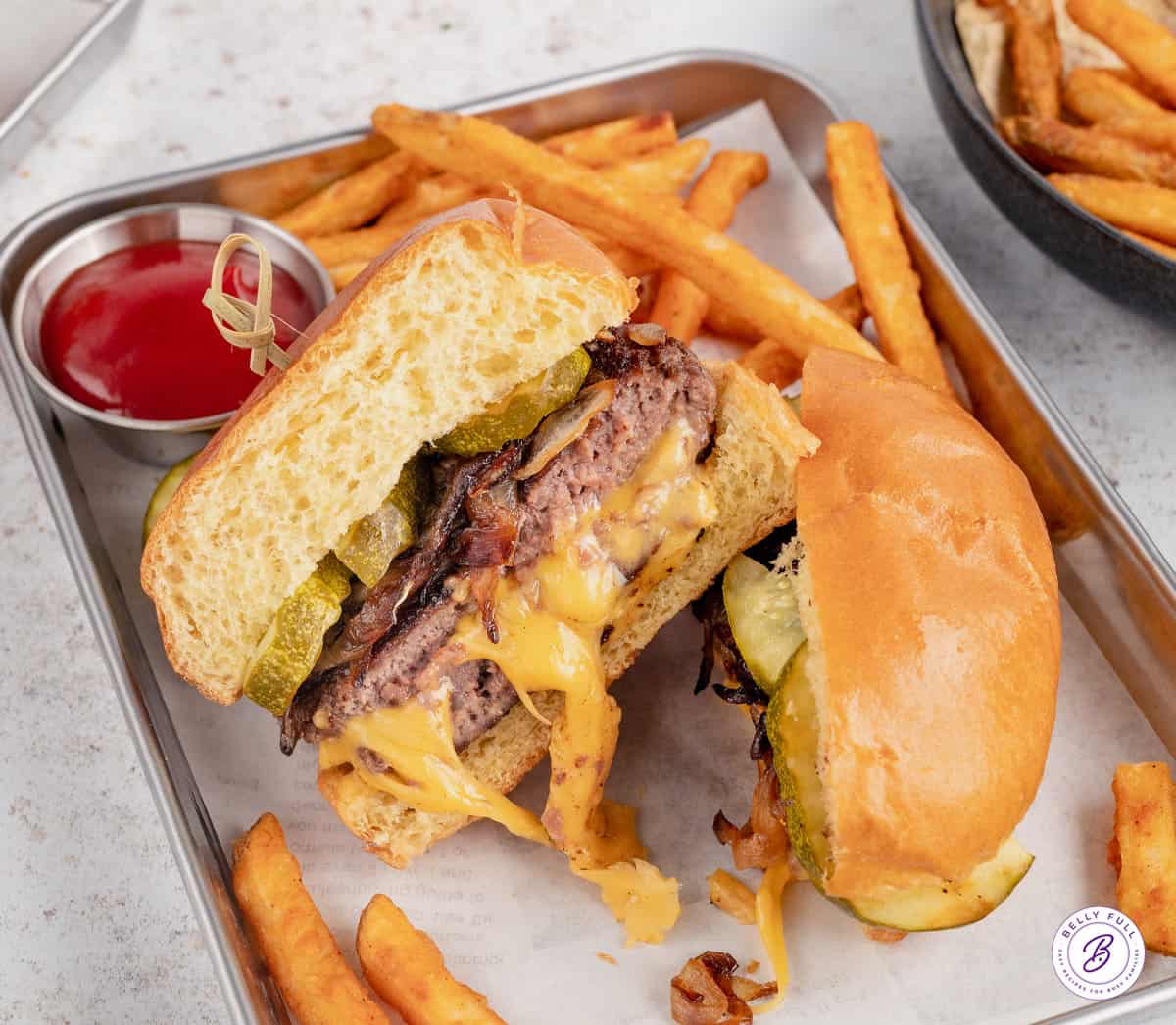 Overhead view of a juicy lucy burger cut in half on a tray with fries