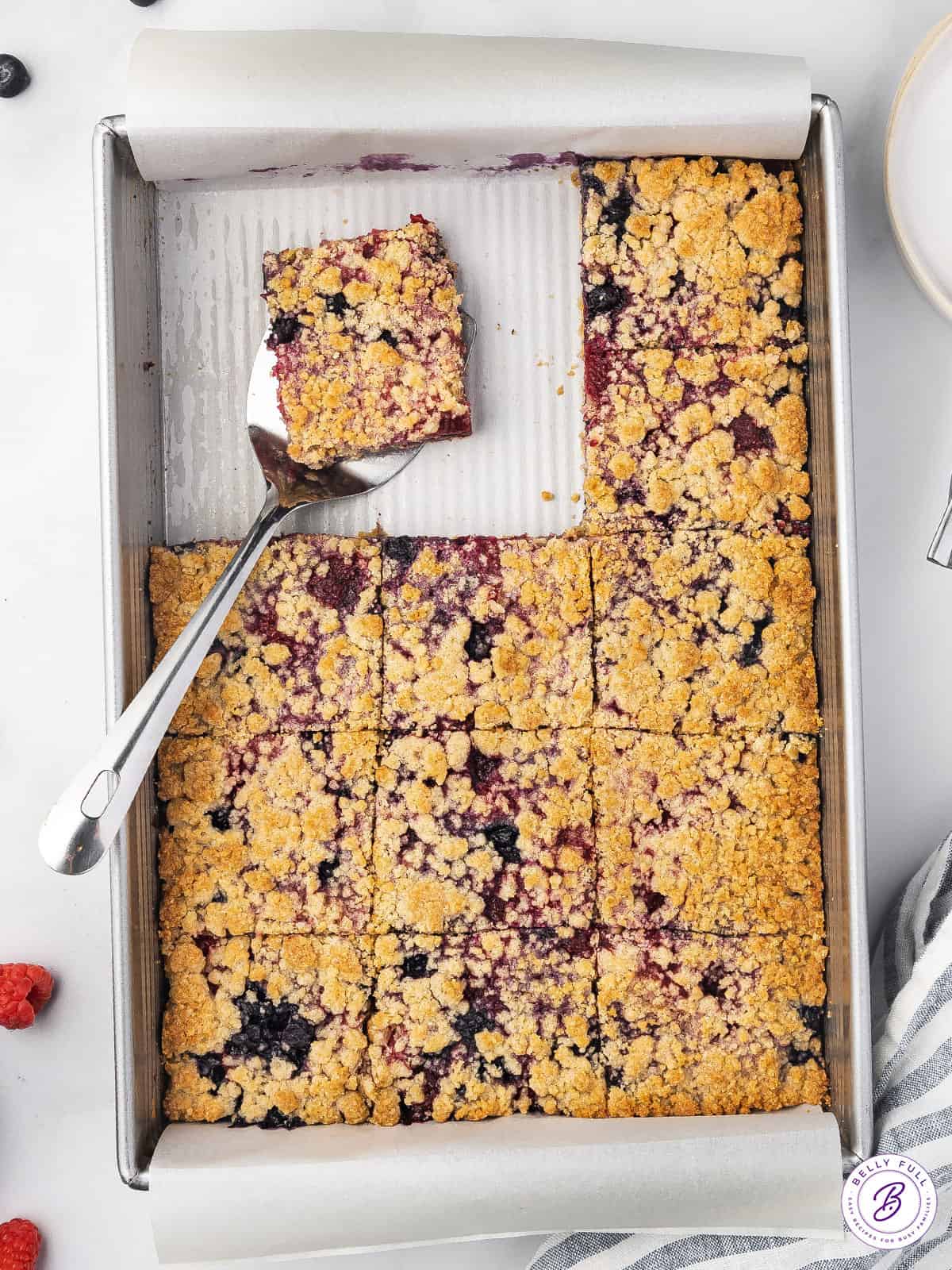 Overhead view of a pan of berry crumb bars, with one on a spatula