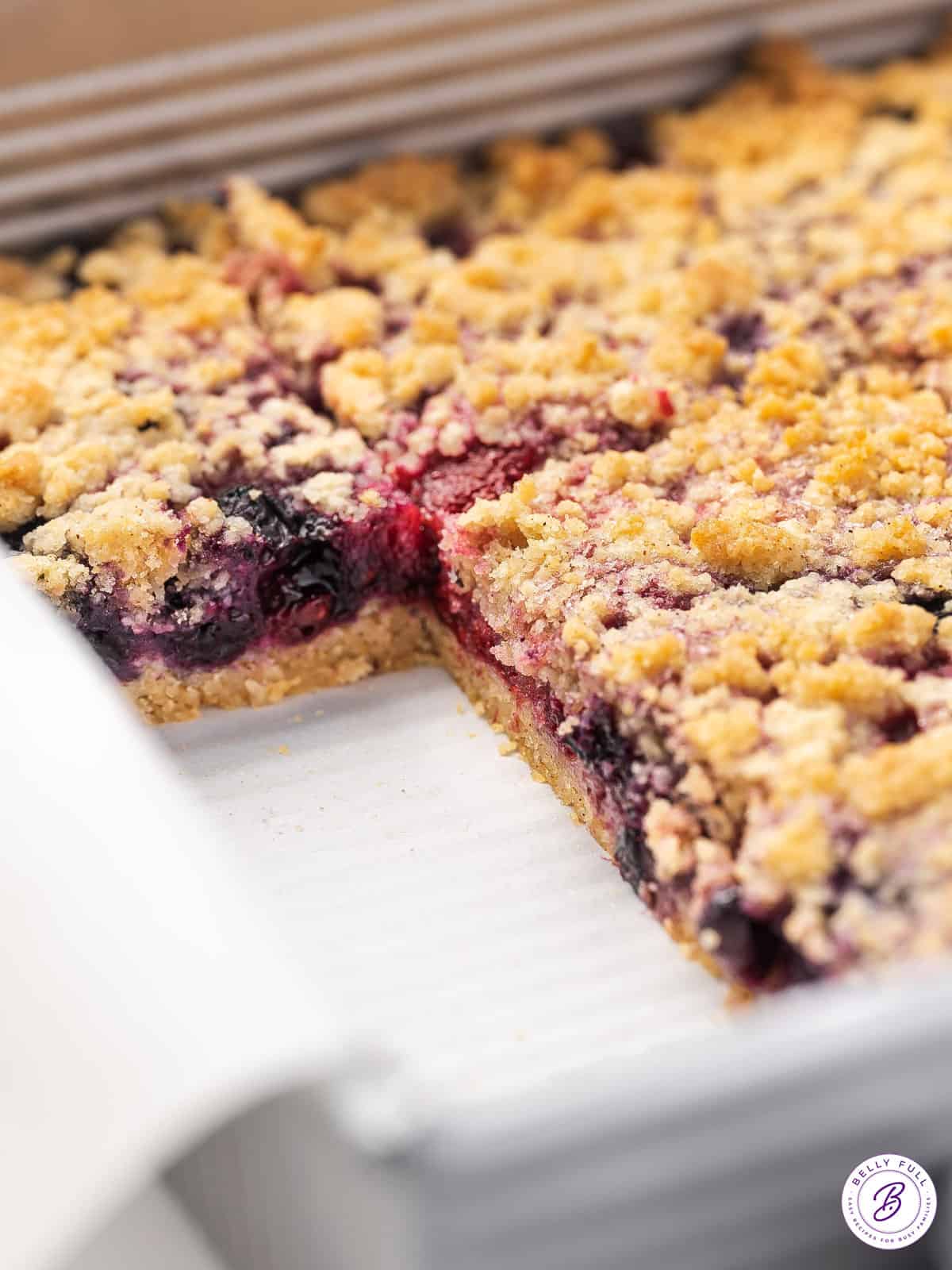 A pan of mixed berry crumble bars, with two pieces missing