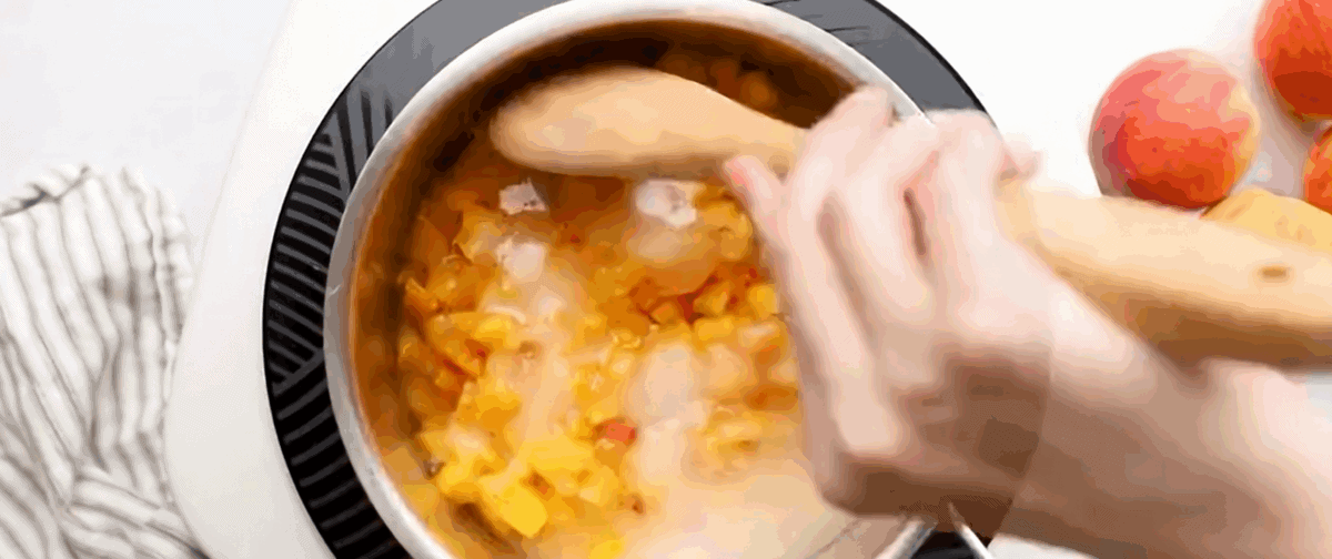 Ingredients to make peach jam being stirred in a pot.