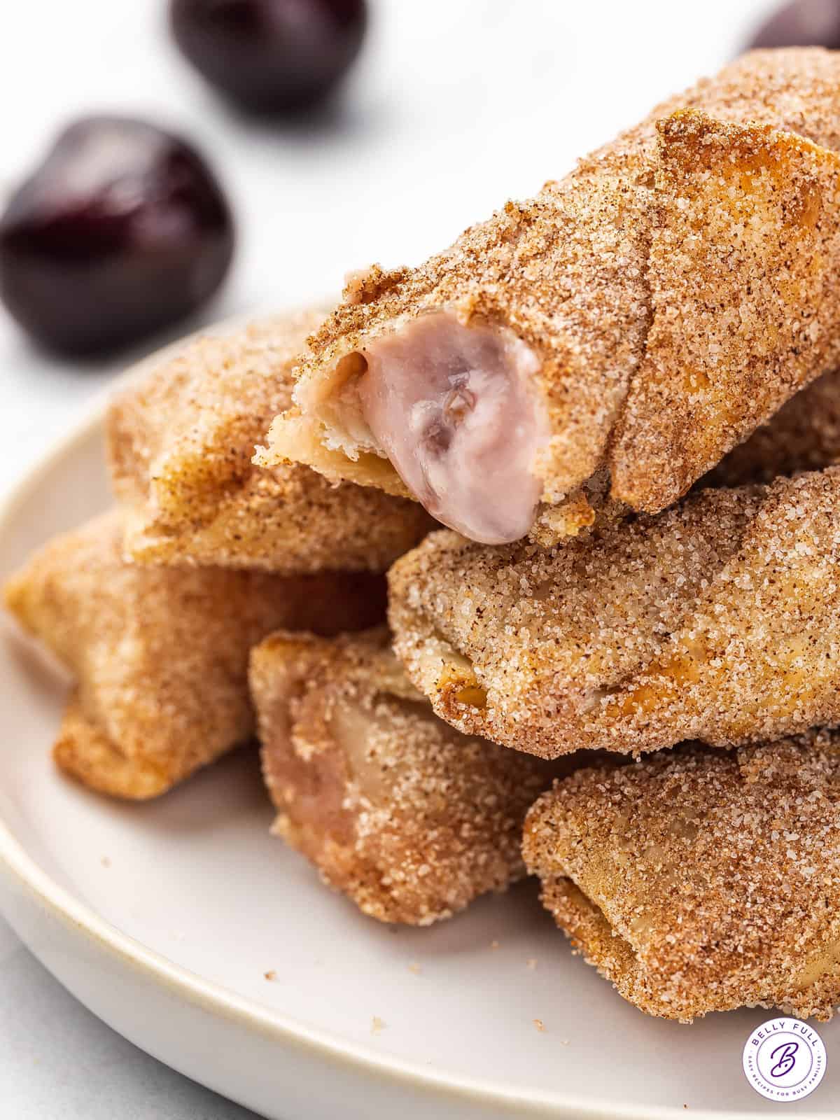 A stack of cherry cheesecake egg rolls, one with the filling showing