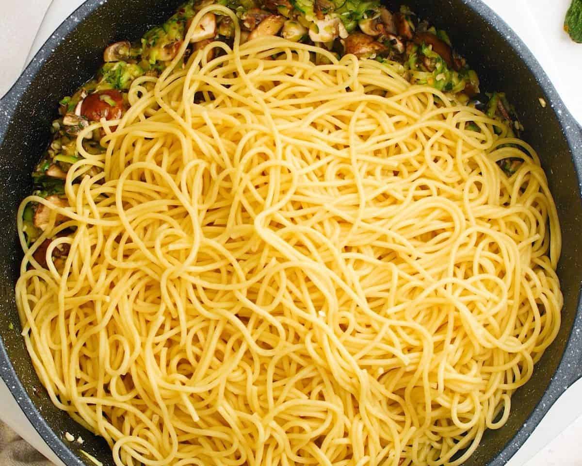 Adding the cooked spaghetti to the pan with the veggies.