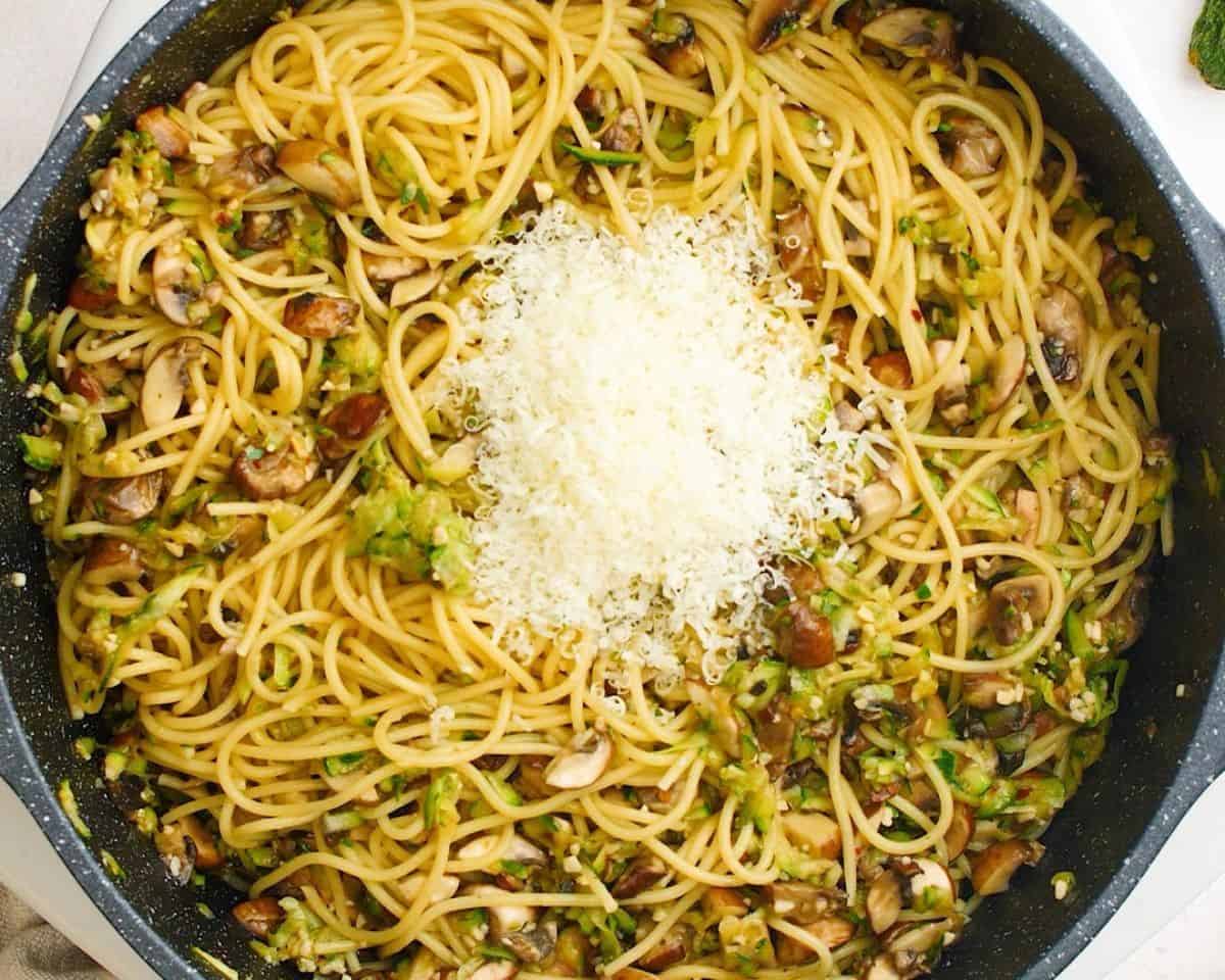 Adding Parmesan cheese to the pasta and veggie mixture.