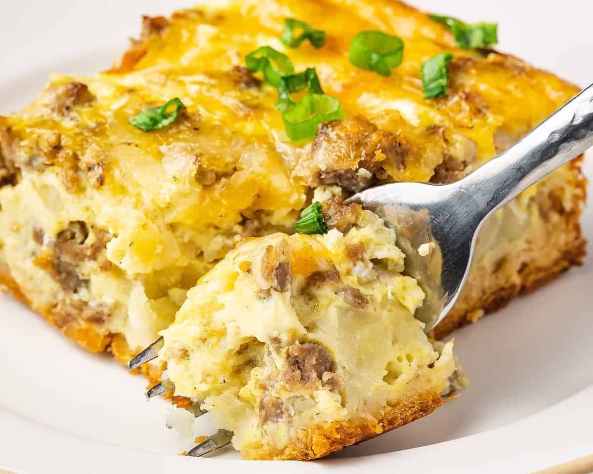 With sausage, hashbrowns, and lots of cheese, this Crescent Roll Breakfast Casserole is an easy breakfast recipe the whole family will love. Slice of crescent roll breakfast casserole on a white plate with a fork, garnished with green onions.