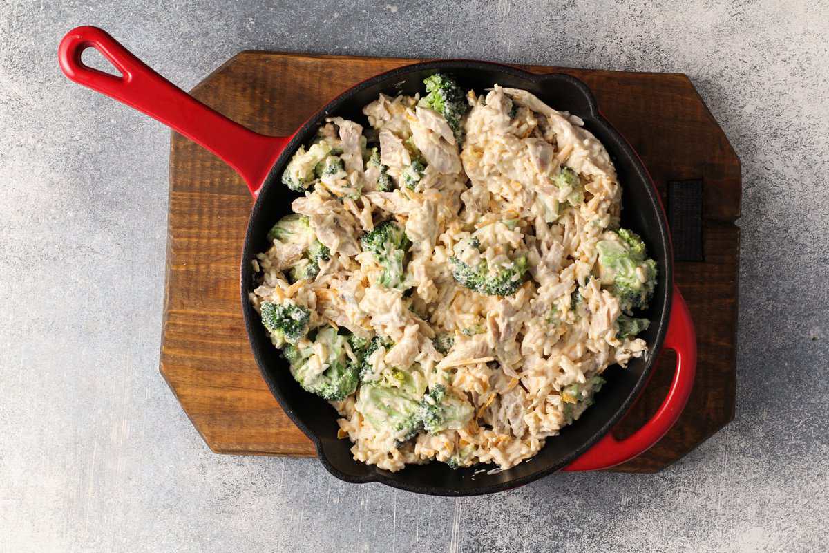 Chicken and broccoli rice casserole ingredients in a red skillet on a wooden cutting board.