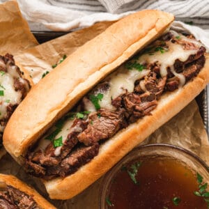 A slow cooker French dip sandwich next to a small bowl of au jus