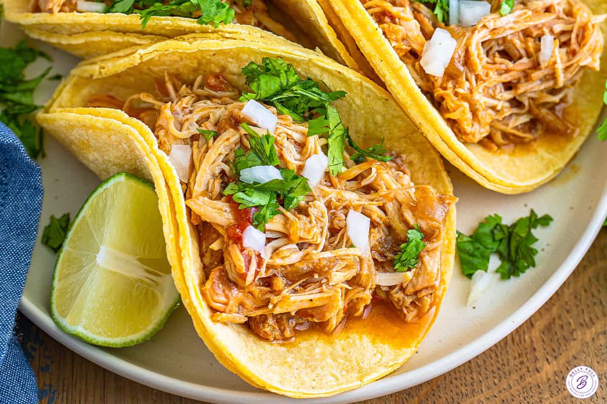 Shredded chicken tacos on a white plate with lime wedges.