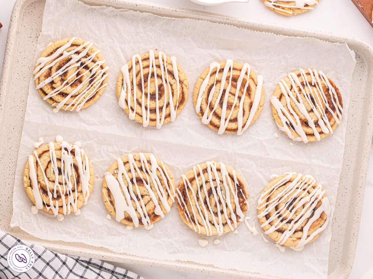 Cinnamon roll cookies with icing drizzled on top on a cookie sheet.