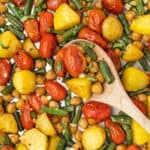 A wooden spoon stirring a veggie sheet pan dinner