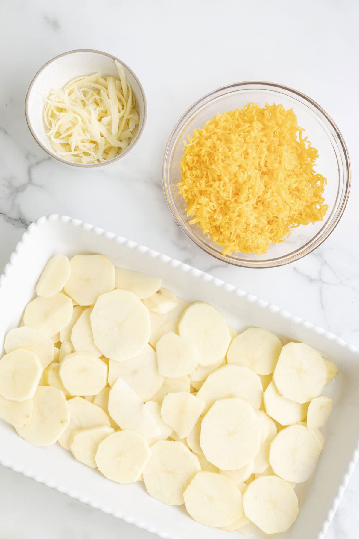 Sliced potatoes layered in a white casserole dish.