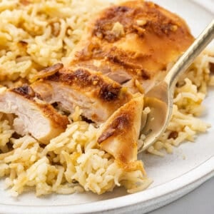 A bite of chicken on a fork with a serving of no peek chicken and rice