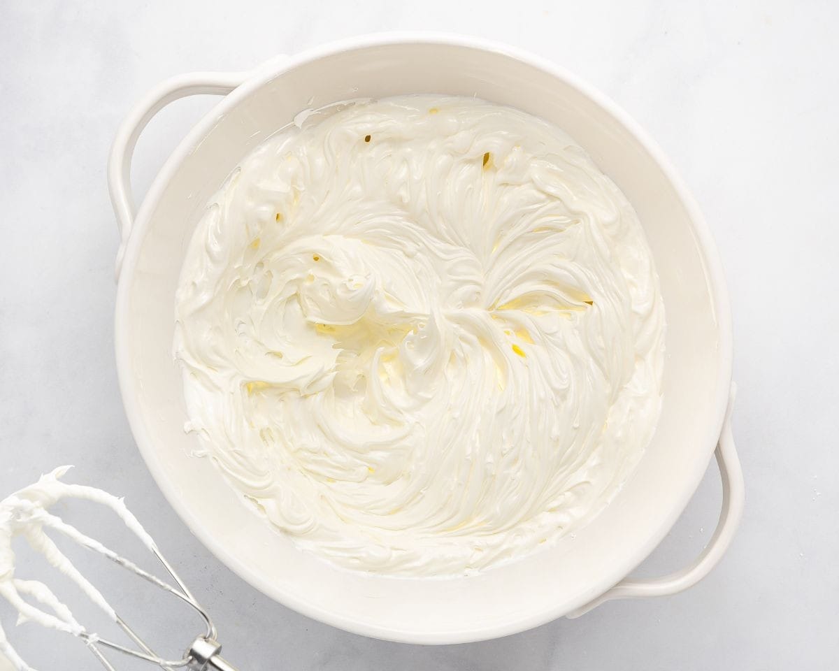 Cream cheese frosting in a white bowl with a whisk next to it.