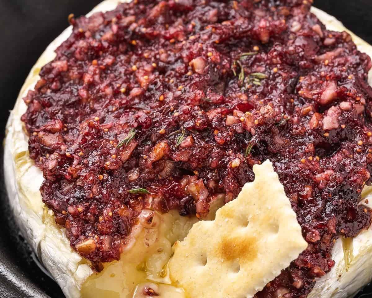 finished baked brie with jam and a cracker being dipped into it