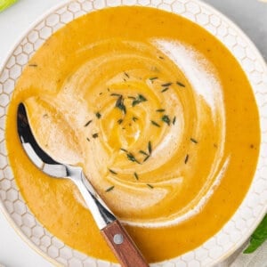 A spoon swirling cream in a bowl of carrot soup