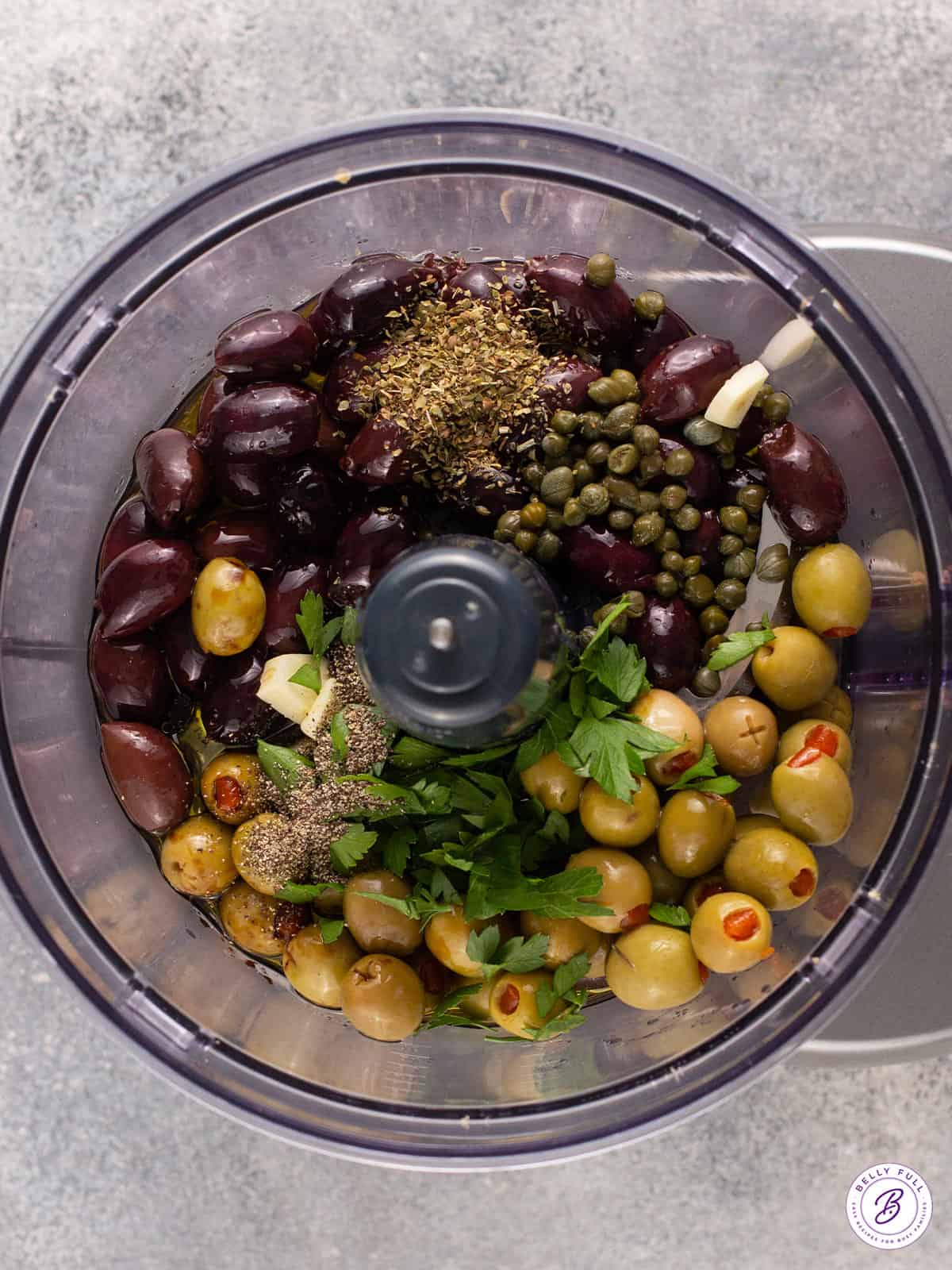 olives, capers, and herbs in a food processor bowl