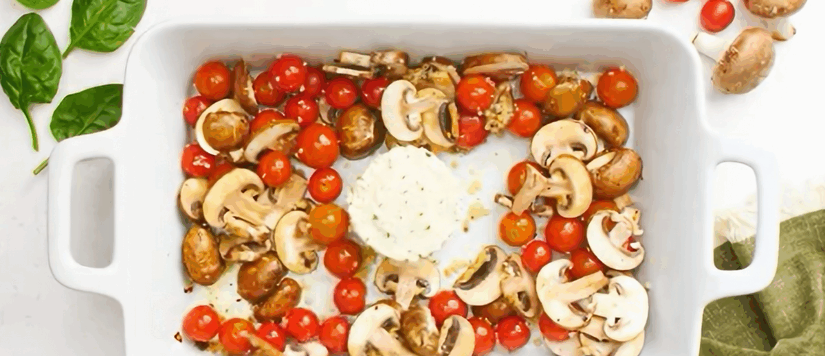 A block of Boursin cheese surrounded by veggies in a white baking dish.
