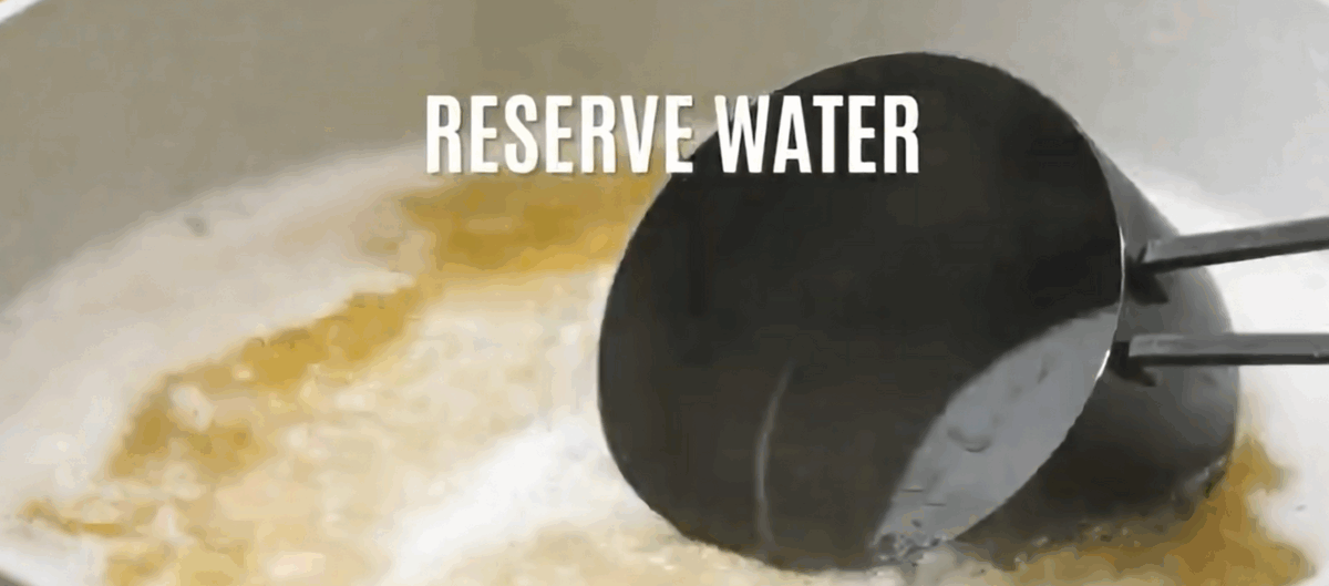 A measuring cup scooping out pasta water from a pot of boiling pasta. 