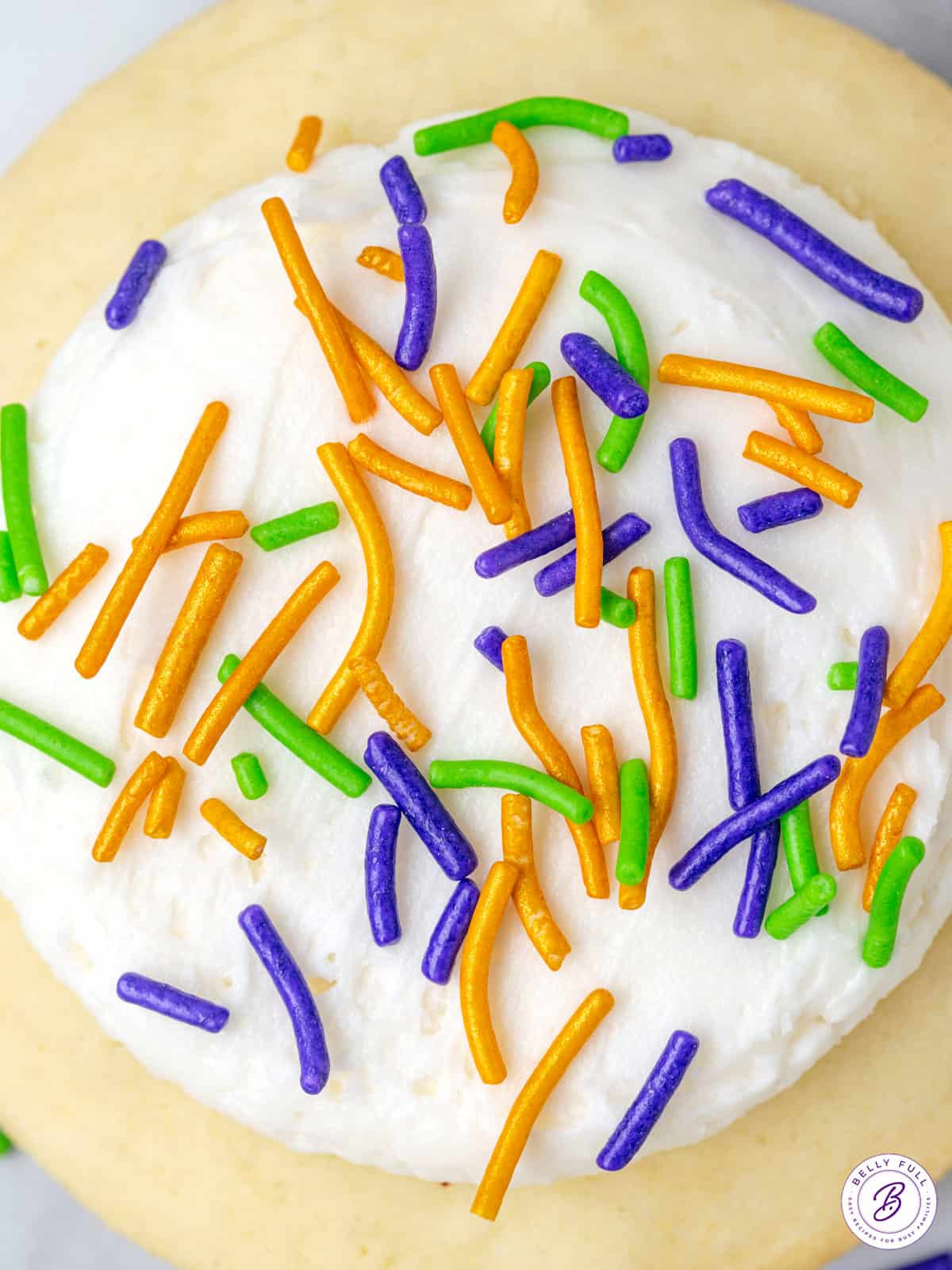 close up frosted cookies with purple, green, and gold sprinkles