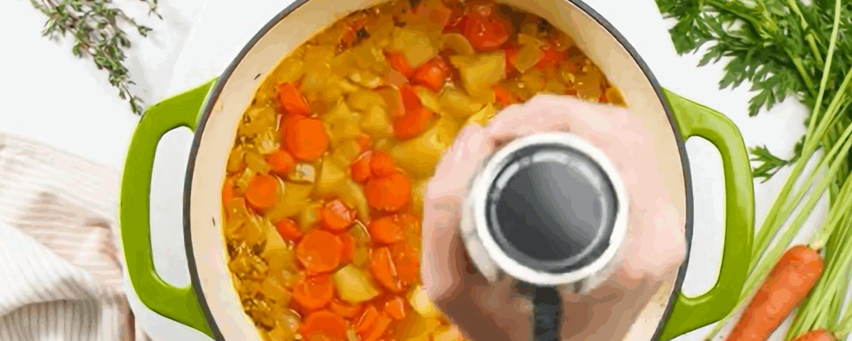 Using an immersion blender to blend the soup.