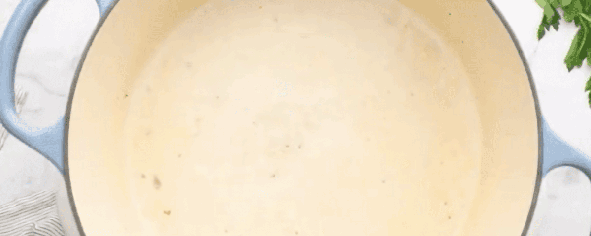 Combining the ingredients to make a roux in a pot with blue handles. 