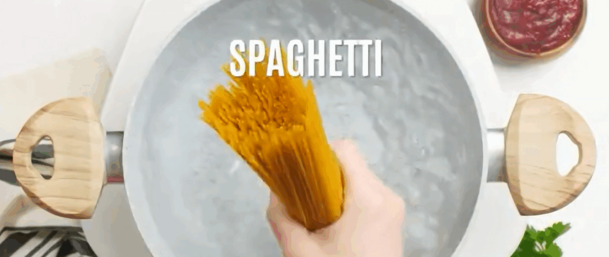 A hand holding spaghetti over boiling water in a pot. 