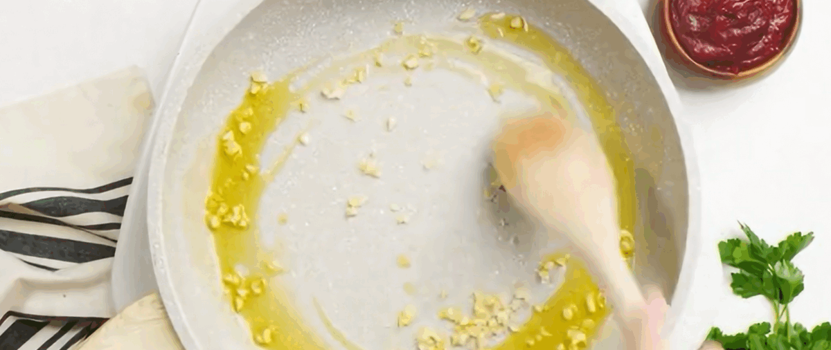 Garlic sauteing in olive oil in a white skillet. 