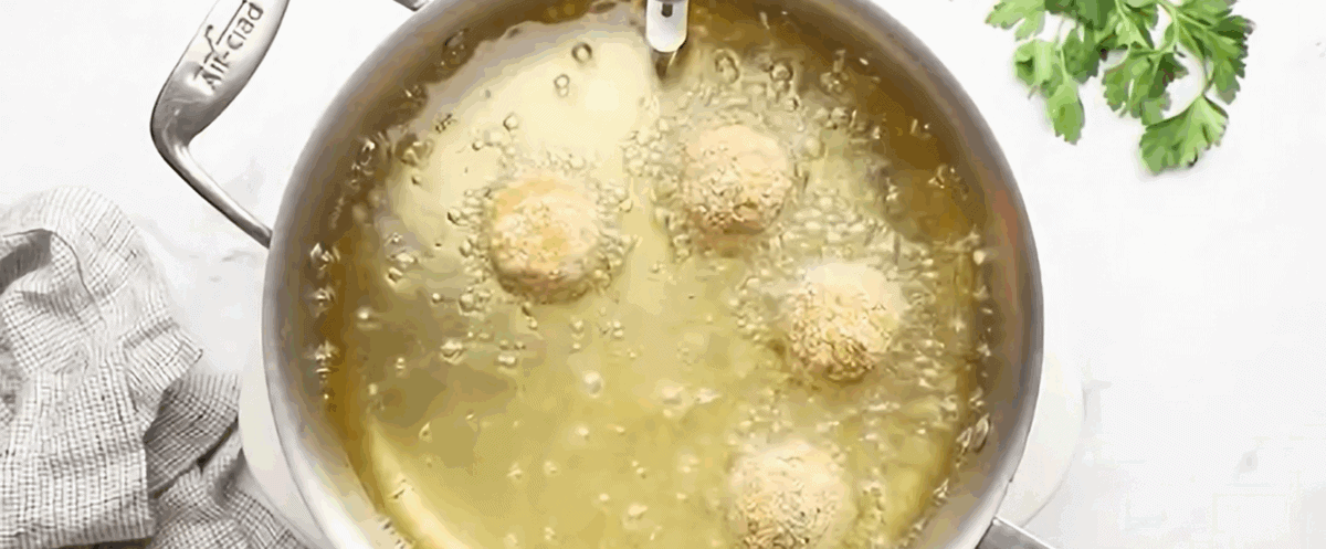 Frying the arancini in a pot of oil.